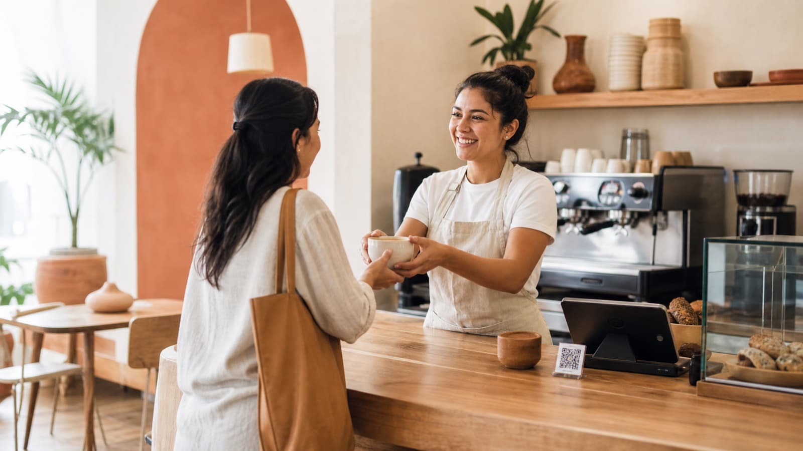 Barista entregando café a una clienta frecuente en una cafetería cálida